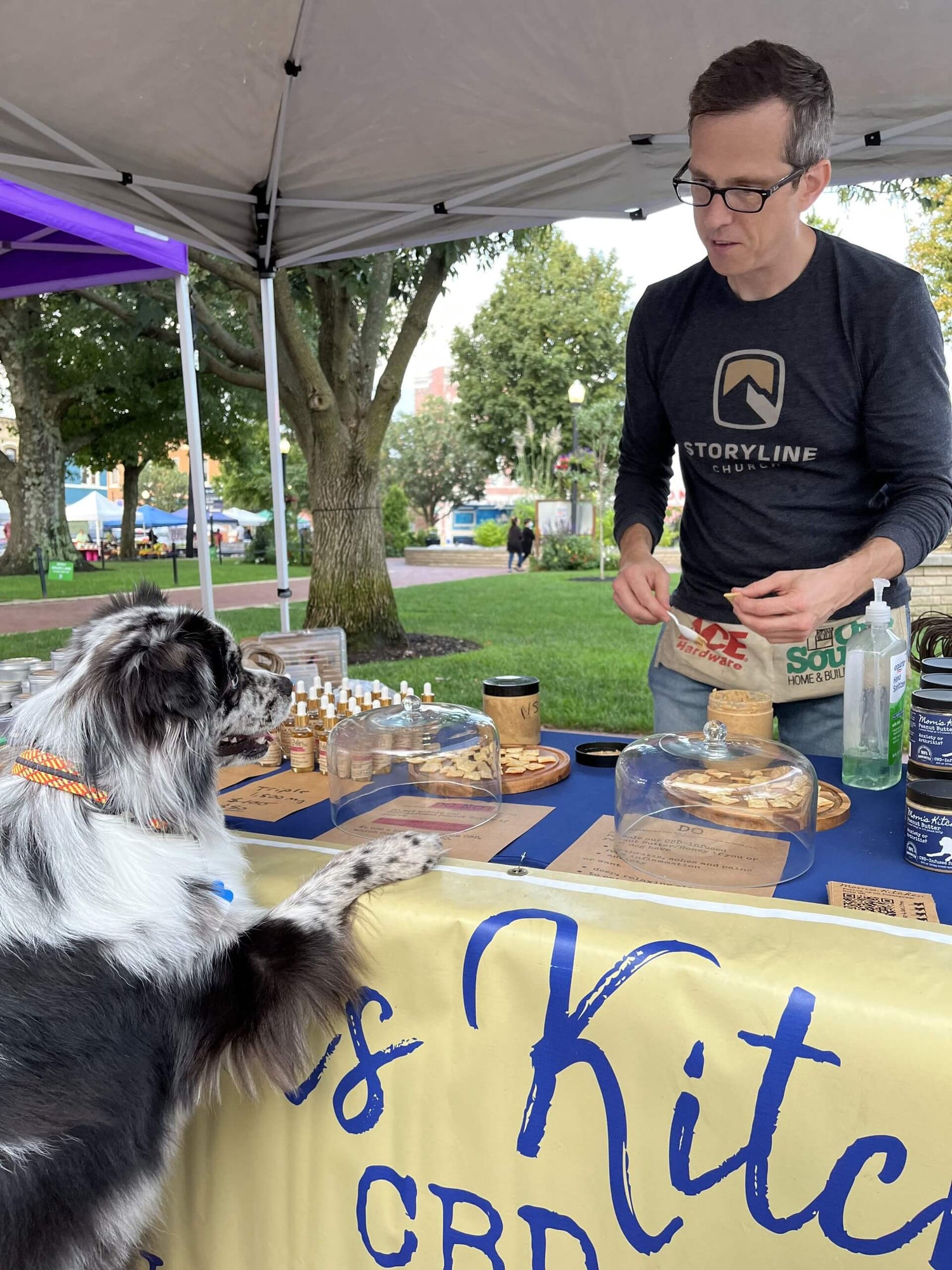 Daniel serving a Peanut Pupper sample to a border collie at the farmers market